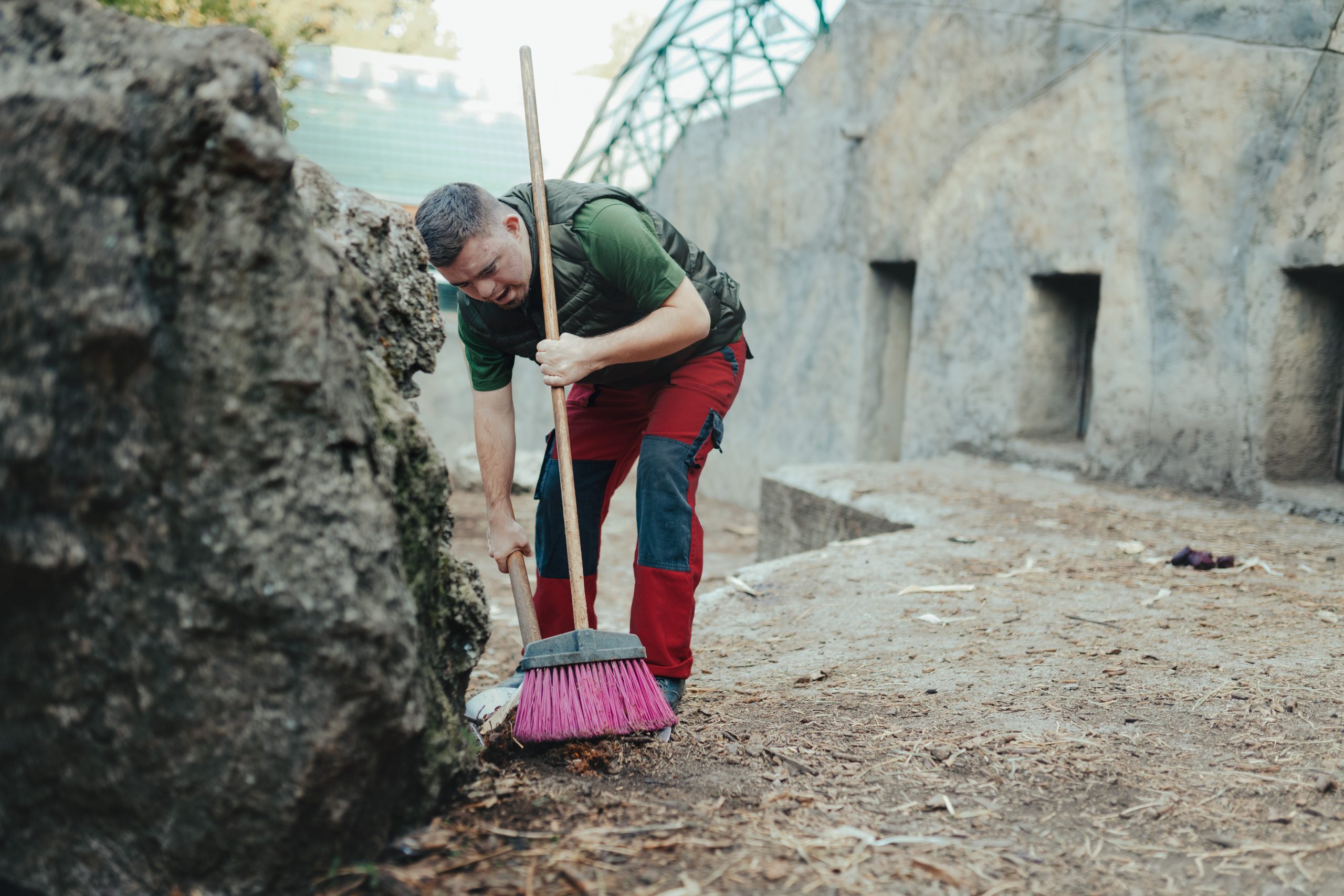 Caretaker with down syndrome in zoo cleaning animal enclosure. Concept of integration people with disabilities into society.